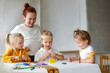 © natalialeb - cheerful teacher woman with a group of cute preschool children at the table draw on paper with multicolored felt-tip pens, montessori and creativity, creative development and lesson in kindergarten