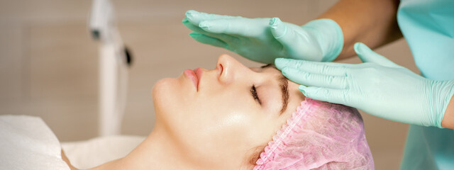 Wall Mural - The woman is having cosmetic treatment during cosmetologist in medical gloves are touching the female face at the spa salon