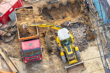 Wall Mural - Excavator digs a hole and loads soil into the back of a truck, aerial top view.