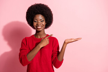 Sticker - Photo of charming dark skin woman point hold hand empty space promoter isolated on pink color background