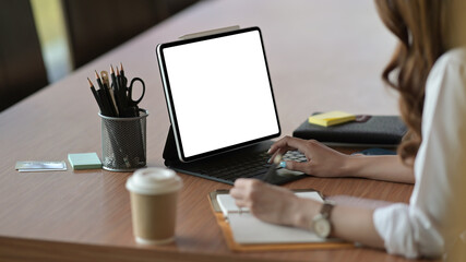 Poster - Behind view of a young office woman taking notes and using a white blank screen digital tablet at the wooden table in the comfortable meeting room.
