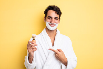 Wall Mural - young handsome man smiling cheerfully, feeling happy and pointing to the side. shaving and foam concept