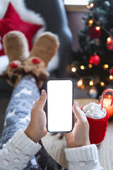 Close up smartphone with empty screen mockup on holiday background with Christmas tree, customer holding phone in hand, shopping online, purchasing gifts, searching information, browsing apps