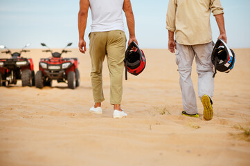 Two racers hold helmets near atvs in desert