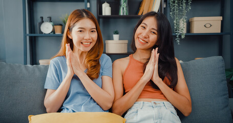 Wall Mural - Teenager couple Asian women feeling happy smiling and looking to camera while relax in living room at home. Cheerful Roommate ladies video call with friend and family, Lifestyle woman at home concept.