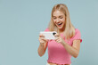© ViDi Studio - Young excited blonde woman 20s wearing casual pink t-shirt using play racing app on mobile cell phone hold gadget smartphone for pc video games isolated on plain pastel light blue background studio