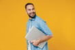© ViDi Studio - Young smiling happy freelancer copywriter satisfied caucasian man 20s wear blue shirt hold closed laptop pc computer look aside on workspace area isolated on plain yellow background studio portrait