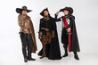 Full-length portrait of thee men in vitage costumes with swords, musketeer and pirate isolated over white background