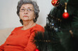 © Sergio - Portrait of lonely sad senior woman with glasses sitting alone at home near xmas tree and looking away. Loneliness in Christmas celebration, self-isolation, lockdown for holiday