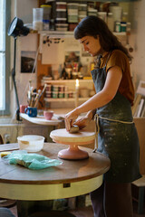 Young woman potter maker work with clay on pottery wheel in creative art space, professional studio. Female artist creating handicraft ceramics for hobby. Relax at handcraft products workshop concept