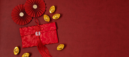 Wall Mural - Chinese new year festival decoration over red background. traditional lunar new year red pokets, gold ingots, paper fans. Flat lay, top view, banner