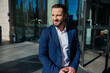 © Taras Grebinets - Handsome successful self-confident young businessman entrepreneur developer in business suit looks aside posing with a luggage on the background of corporate modern high-rise building glass entrance