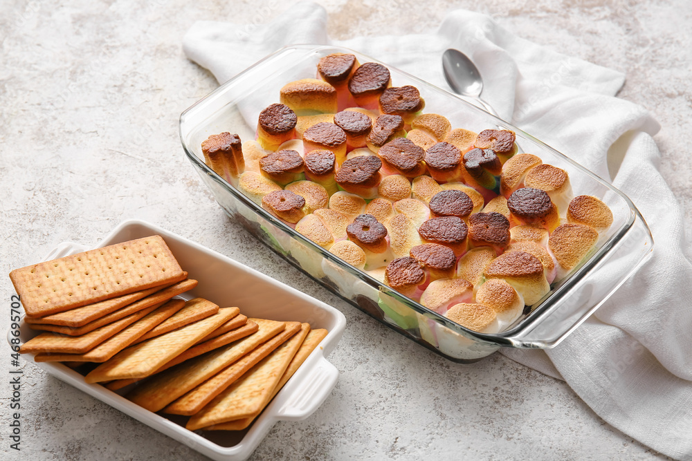 Baking dish with delicious S'mores dip and crackers on light background