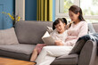© Blue Jean Images - Young Chinese mother and daughter reading book at home