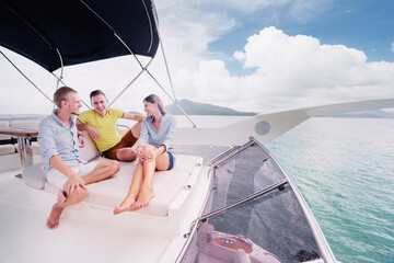 Wall Mural - Friendship and vacation. Group of laughing young people sitting on the yacht deck sailing the sea.