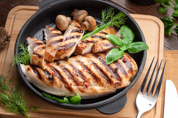 Wall Mural - Roasted chicken fillet and mushrooms with herb in the frying pan on the wooden table close-up.