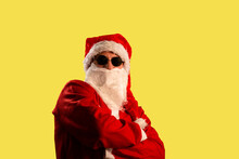 Santa Claus Wearing Round Sunglasses With Crossed Arms Looking Directly In A Camera; Isolated Portrait On Yellow Background.