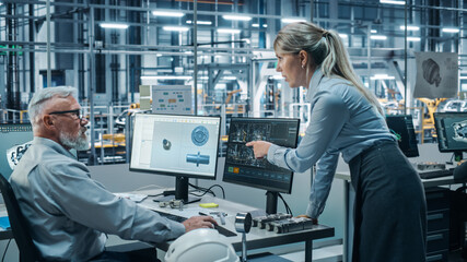 Wall Mural - Car Factory Office: Female Project Manager Talks to Male Chief Automotive Engineer Working on Computer. Monitoring, Control, Equipment Design. Automated Robot Arm Assembly Line Manufacturing Vehicles