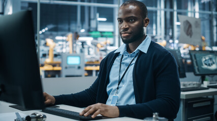 Wall Mural - Car Factory Office: Portrait of Confident Black Male Chief Engineer Working on Desktop Computer. Professional Technician in Automated Robot Arm Assembly Line Manufacturing High-Tech Electric Vehicles