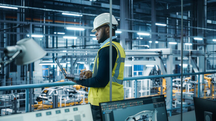 Leinwandbilder - Car Factory: Professional Male Automotive Engineer Wearing Hard Hat, Walking, Using Laptop. Monitoring, Control, Equipment Production. Automated Robot Arm Assembly Line Manufacturing Electric Vehicles