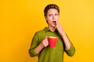 Wall Mural - Photo of tired sleepy lady hold cup yawn look empty space wear green shirt isolated yellow color background