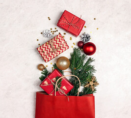 Red paper shopping bag with Christmas decorations, gifts and fir branch on light marble background.