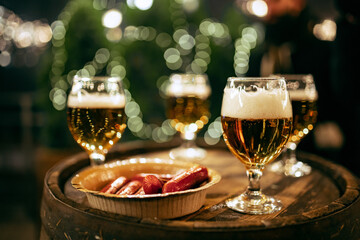 Close-up glasses of light frothy beer and sausages on wooden old barrel roll. Concept of drinks, fun, meeting, oktoberfest, winter fair