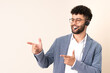 © luismolinero - Telemarketer Moroccan man working with a headset isolated on beige background pointing finger to the side and presenting a product