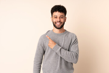 Young Moroccan man isolated on beige background pointing to the side to present a product