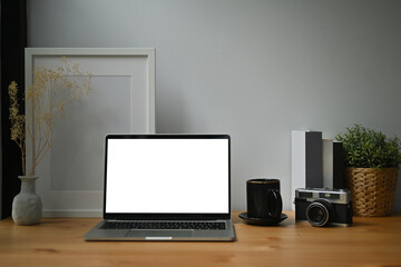 Poster - Photo of a white blank screen computer laptop on the wooden table surrounded by a coffee cup, vintage camera, empty picture frame potted plant and books.