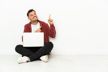 Wall Mural - Young handsome caucasian man sit-in on the floor with laptop pointing with the index finger a great idea