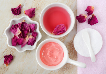 Two small white bowls with rose water (toner) and jelly rose mask. Dry rose petals, cotton pad. Ingredients for preparing homemade cosmetics. Natural beauty treatment recipe, zero waste concept.