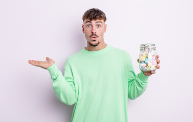 Wall Mural - young handsome man looking surprised and shocked, with jaw dropped holding an object. jelly candies concept