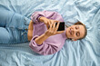 leisure, children and technology concept - happy smiling girl in earphones with smartphone lying on bed at home