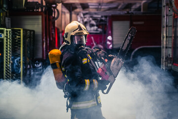 Wall Mural - Portrait of young fireman standing and holding a chainsaw in the middle of the chainsaw's smoke  .