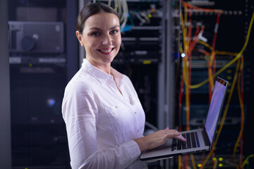 Portrait of caucasian female engineer smiling while using laptop in computer server room