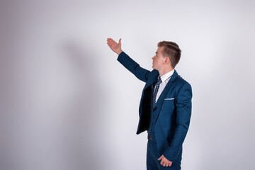 An intelligent man in a business suit points to the side while standing with his back to the camera. Guy on a gray background.