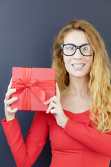 Wall Mural - Girl in glasses with a red gift box. Holiday gift. The lady in red is holding a gift. Holiday poster