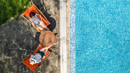 Wall Mural - Young girls relax near swimming pool in sunbed deckchairs, women friends have fun on tropical vacation in hotel resort, aerial top view from above
