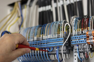 Wall Mural - an electrical engineer uses an insulated screwdriver to connect the equipment in the control panel t