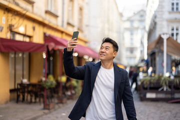 Wall Mural - Asian businessman recording video on smartphone while walk in old city. Concept video blogging and business travel. Adult man wear suit