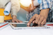 © Vittaya_25 - construction worker team planning about building plan with digital mobile tablet on blueprint and construction tool on conference table at construction site, contractor, business, construction concept