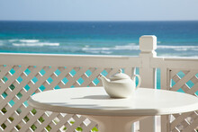 White Teapot On A White Table Against A Blue Sea Background. Selective Focus On Teapot