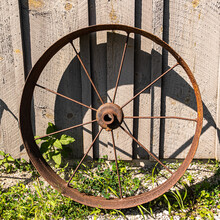 Old Rust Covered Wagon Wheel - Wagon Wheel From Old Farm Equipment Leaning Against A Barn Wall In Early Afternoon Sunlight.