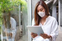 A Young Woman Wearing Protective Face Mask, Holding And Using Digital Tablet For Healthcare And Coronavirus Concept