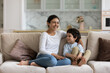 © fizkes - Laughing Indian mom enjoying leisure time with happy son at home, talking to boy. Mother and cheerful preschool child having fun together, relaxing on couch. Babysitter watching cute kid