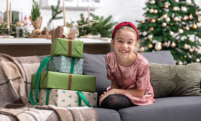 Wall Mural - A little girl enjoys a lot of Christmas gifts sitting on the couch at home.