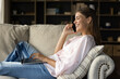 © fizkes - Smiling young beautiful woman using computer, involved in pleasant cellphone conversation, enjoying communicating distantly, shopping online or discussing news working remotely on project at home.