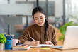 © amnaj - Pretty young Asian businesswoman working on laptop and taking notes In office..