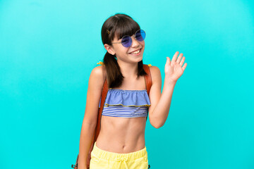 Little caucasian kid going to the beach isolated on blue background saluting with hand with happy expression